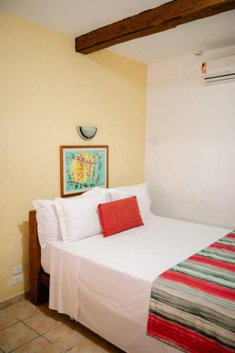 a bedroom with a white bed with a red pillow at Hotel Pousada Tambayba in Maresias