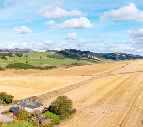 an aerial view of a field with a farmhouse in the foreground at Hillockbrae in Bridgend of Lintrathen