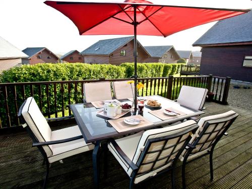 a table with a red umbrella on a deck at Ash Lodge - Retallack in Saint Columb Major