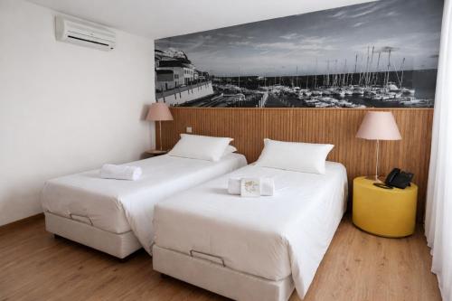 two beds in a hotel room with a picture on the wall at Hotel Zenite in Angra do Heroísmo