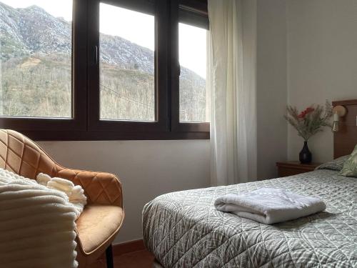 a bedroom with a bed and a chair and two windows at La Paserina in Arenas de Cabrales