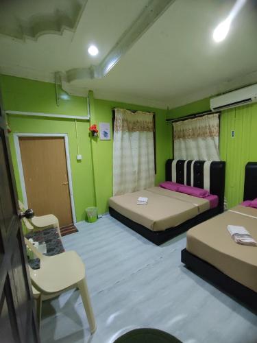 a green room with two beds and a chair at Mokdo Guest House in Perhentian Islands