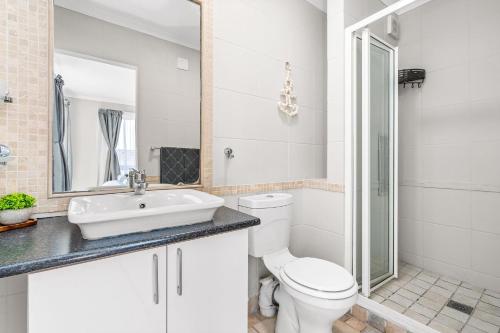 a white bathroom with a toilet and a sink at Coral Grove in Strand