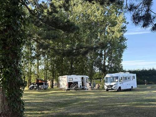 two rvs parked in a field next to trees at Camping Le Romantic in Steenvoorde