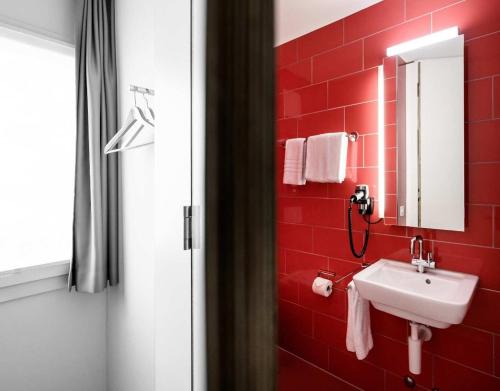 a red tiled bathroom with a sink and a mirror at Hotel Bauernhof - Self Check-In Hotel in Rotkreuz
