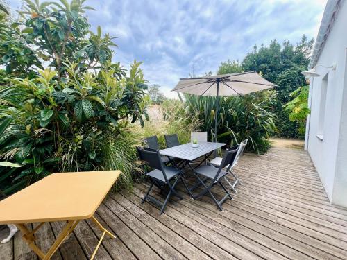 a wooden deck with a table and chairs and an umbrella at Maison Aquitaine "Tanchet" in Les Sables-d'Olonne