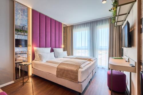 ein Schlafzimmer mit einem großen Bett und einer lila Wand in der Unterkunft VOYA Hotel in Ringsheim