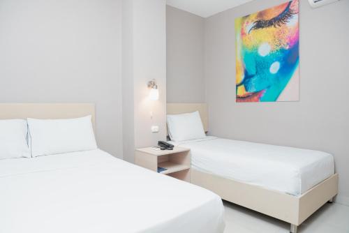 two white beds in a white room with a painting at Ribai Hotels -Riohacha in Ríohacha