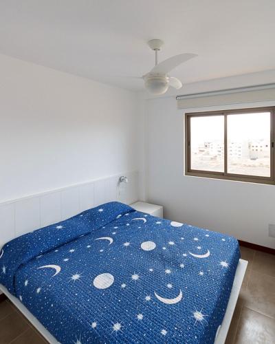 a bedroom with a bed with a blue comforter and a window at Pousada do Norte, ilha do Fogo in Calheta