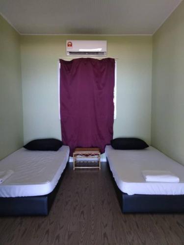 two beds in a room with a purple curtain at Kudat Beach House 4 in Kudat