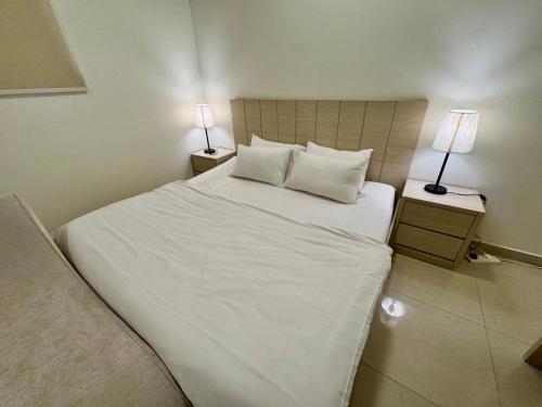 a bedroom with a large white bed with two lamps at اكنان للشقق المفروشة in Buraydah