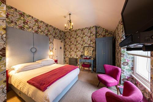 a bedroom with a bed and two pink chairs at Escape Boutique B&B in Llandudno