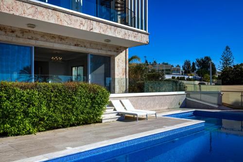 a chair sitting next to a swimming pool next to a building at Olymp Luxury Villa А - Beachfront Luxury Living in Kissonerga