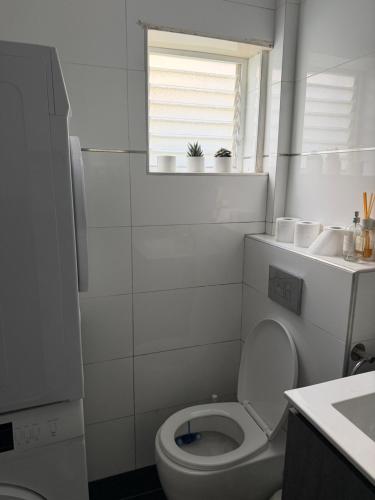a white bathroom with a toilet and a window at The Urban Suite in Petaẖ Tiqwa