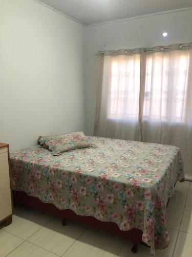 a bedroom with a bed with a floral bedspread and a window at Hostel Hotel uma otima opçao para suas ferias e um bom descanso in Cianorte