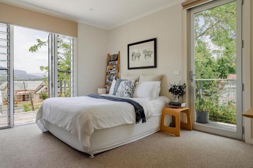 a bedroom with a white bed and large windows at The Tailor's Terrace, Kangaroo Valley in Kangaroo Valley