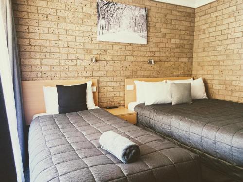 a bedroom with two beds and a brick wall at Muswellbrook Motor Inn in Muswellbrook