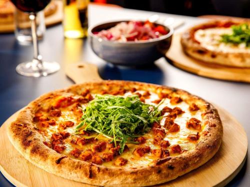 a pizza on a wooden plate with a salad on it at ibis Budget Terminal 2 Manchester Airport by Accor in Hale