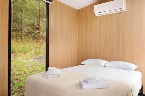 two towels on a bed in a room with a window at Wombat Hideaway by Tiny Away in Laguna