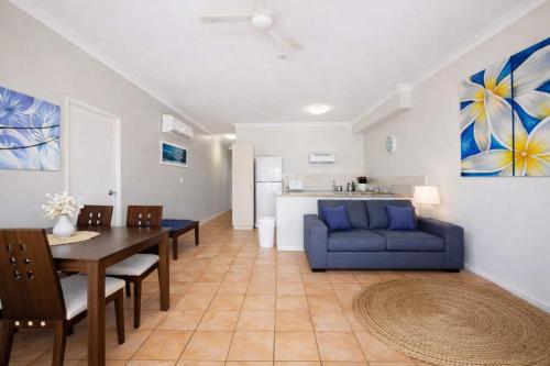 a living room with a blue couch and a dining table at The Anchorage Escape Apartment - Steps away from City, Ferry and Stadium Townsville in Townsville