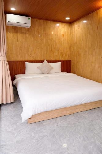 a bedroom with a white bed with a wooden wall at Kingfisher Nest in Hai Phong