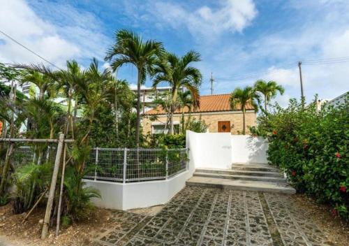 a house with palm trees and a white fence at Miyakojima Villa Charles in Miyako-jima