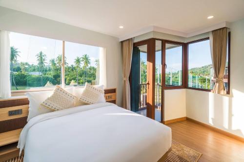 a bedroom with a white bed and large windows at Wyndham Garden Samui Wing in Chaweng