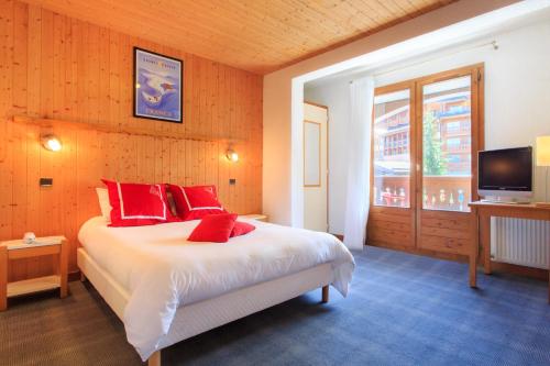 a bedroom with a bed with red pillows and a television at Hotel Club Blanche Neige in Courchevel