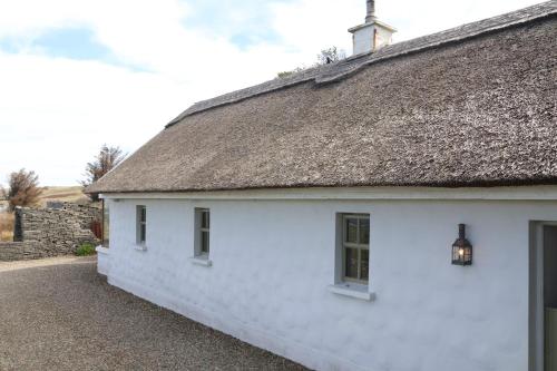a white cottage with a thatch roof at Storytellers Cottage in Doolin