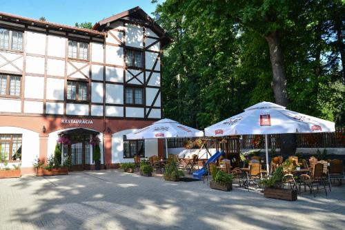 two umbrellas and tables and chairs in front of a building at Hotel Camelot in Szczawno-Zdrój