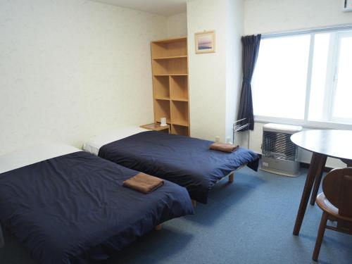 two beds in a room with a table and a window at Guest House Moshiripa in Wakkanai