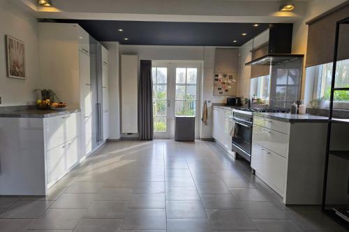 a large kitchen with white cabinets and a tile floor at Wellness Villa voor 6 personen incl Sauna & Hottub in Meerssen