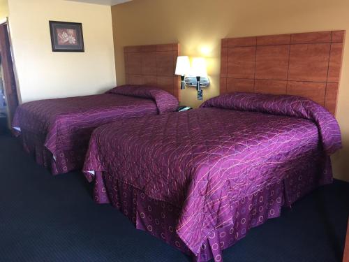 2 letti in una camera d'albergo con coperte viola di Royal Inn Pearsall a Pearsall