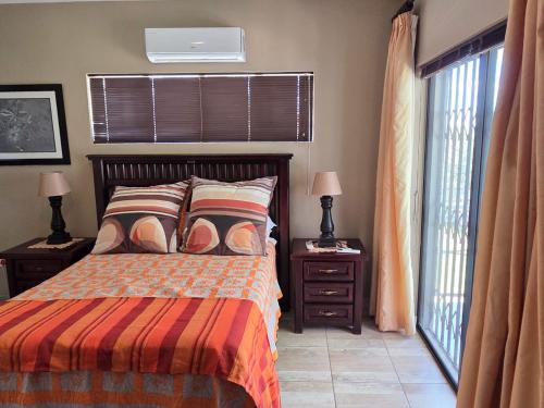 a bedroom with a bed with two night stands and two windows at Klaas Vakie Guesthouse in Beaufort West