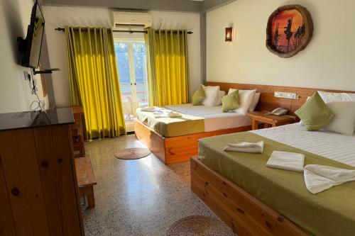 a bedroom with two beds with yellow curtains and a television at Jkl MahaOya Villa in Wayikkal