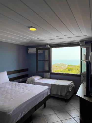 a bedroom with two beds and a large window at Pousada Mirante dos Papagaios in Búzios