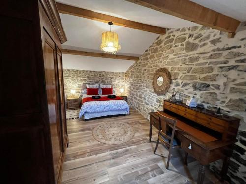 a bedroom with a bed and a piano in a stone wall at Le Mas Vivarés in Lablachère