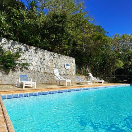 a swimming pool with two chairs and a stone wall at The Eco Palace Hostel in Búzios