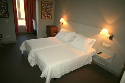 1 dormitorio con 1 cama blanca grande y 2 lámparas en La Posada del Rancho en Segovia