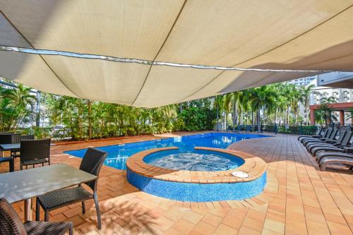 an umbrella over a pool with chairs and a table at Mantra on The Esplanade in Darwin