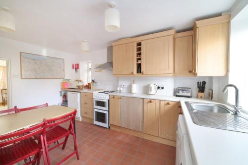 a kitchen with wooden cabinets and a table with red chairs at Beautiful Cottage & Garden Quantock Hills in Nether Stowey
