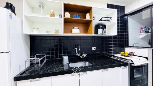 a kitchen with a sink and a black tiled wall at Apartamento Centro Ubatuba - Ubatuba House Temporada in Ubatuba