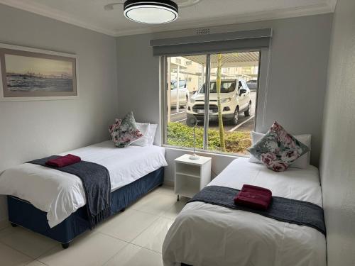 a bedroom with two beds and a window with a car outside at 34 Laguna La Crete in Uvongo Beach