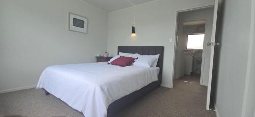 a bedroom with a white bed with a red pillow on it at Beachfront Bliss in Snells Beach