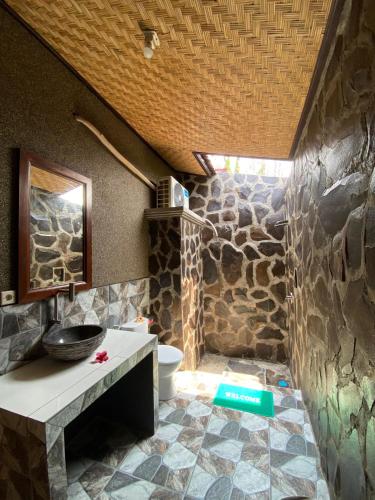 a bathroom with a stone wall and a toilet at Mango Moon in Pemuteran