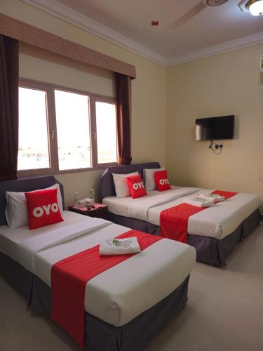 a hotel room with three beds with red pillows at Ras Al Hadd Guest House in Al Ḩadd