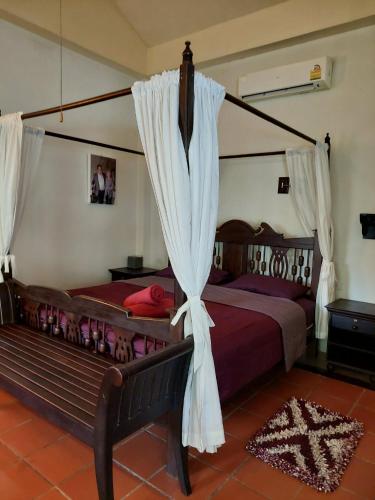 a bedroom with a canopy bed and a bench at Baan Rim Tarn B&B in Takua Pa