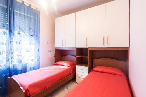 two beds in a bedroom with white cabinets and red sheets at Annie's Home in La Giustiniana