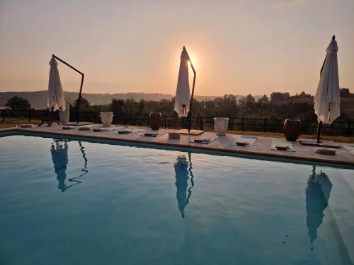 a swimming pool with umbrellas and chairs and the sunset at Pure Gardères in Monlezun