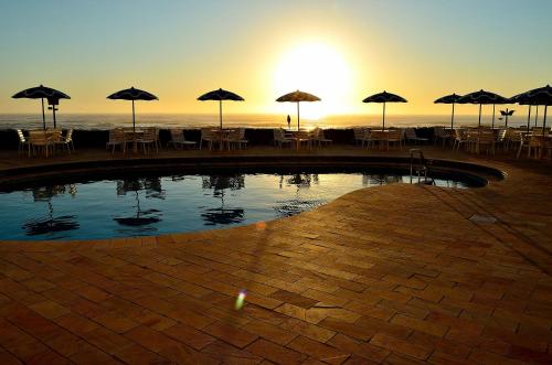 a pool with tables and umbrellas on the beach at Dunas Praia Hotel in Torres